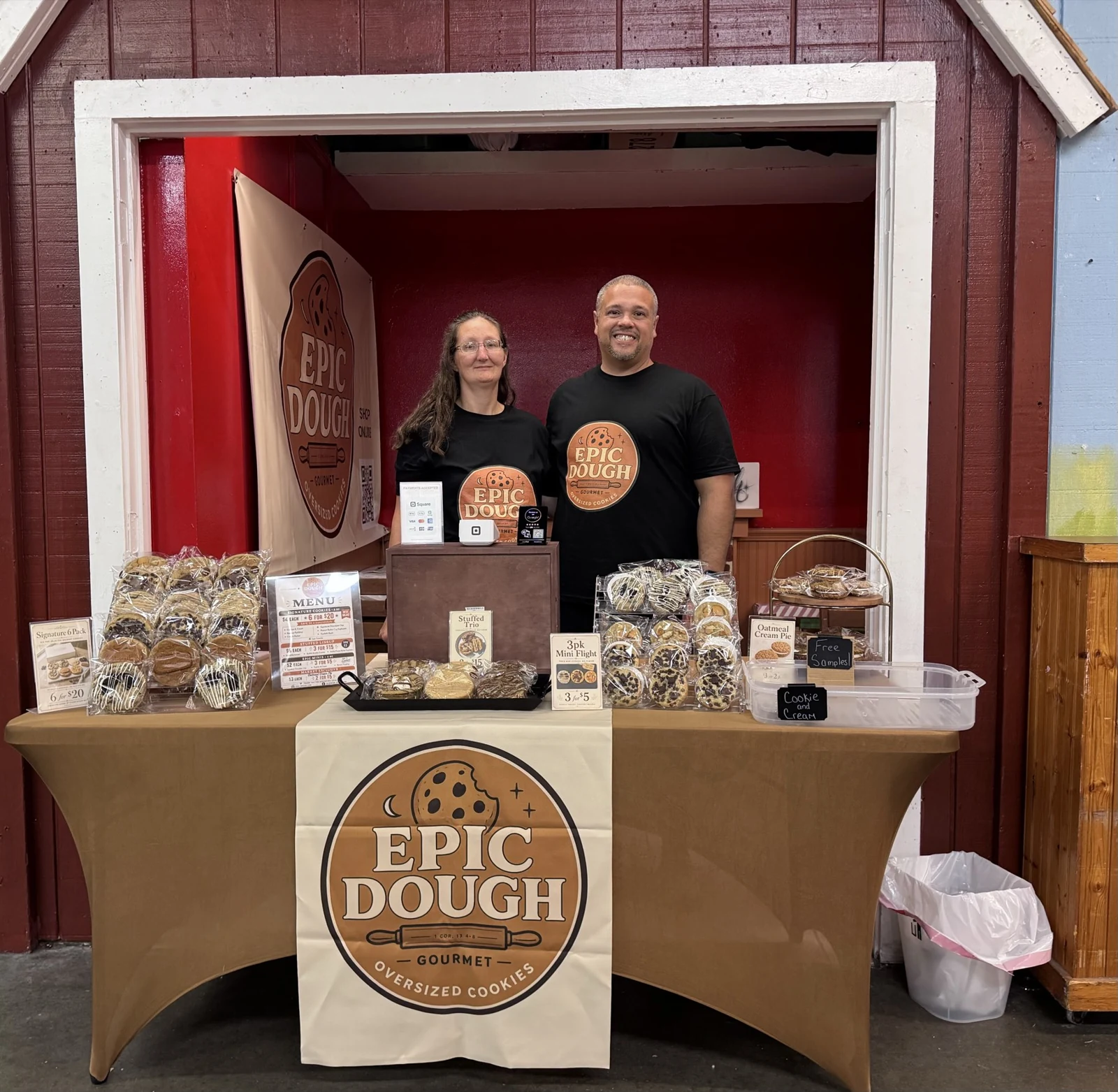 The Epic Dough market booth, with two people standing behind a table of packaged cookies under an Epic Dough banner.
